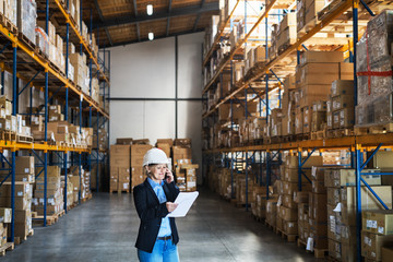 Senior woman warehouse manager or supervisor with tablet and smartphone, making a phone call.