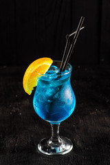 Fresh blue cocktail with orange and ice on black background