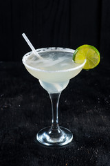 Alcohol transparent cocktail with ice and lime on black background