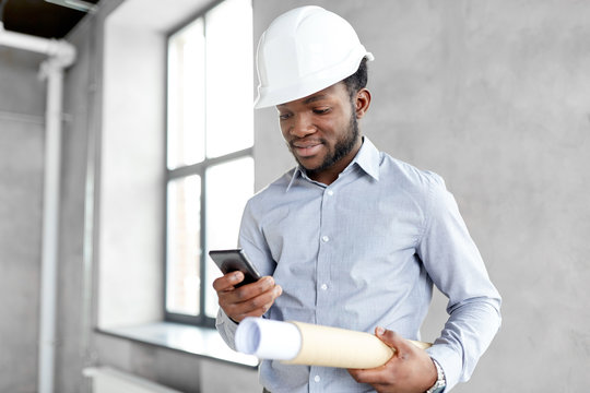 architecture, construction business and people concept - african american architect in helmet with blueprint and smartphone