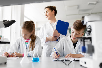Fototapeta na wymiar education, science and children concept - teacher and students studying chemistry at school laboratory and writing to workbooks