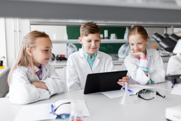 education, science and technology concept - kids with tablet pc computer studying biology or chemistry at school laboratory