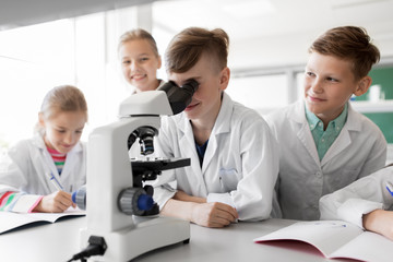 education, science and children concept - kids or students with microscope studying biology at school laboratory