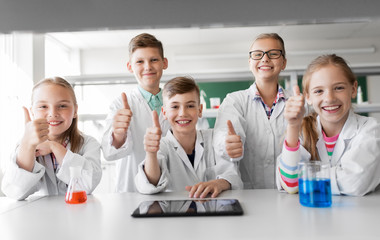 education, science and technology concept - happy kids with tablet pc computer and test tubes studying chemistry at school laboratory and showing thumbs up
