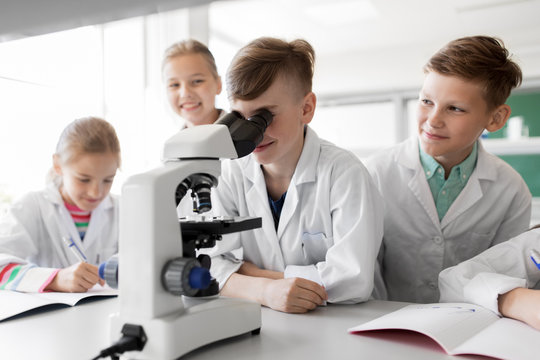 education, science and children concept - kids or students with microscope studying biology at school laboratory - Powered by Adobe
