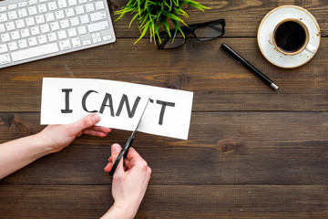Self confidence concept. Hands cutting the letter t of written word I can't by sciccors. Office desk. Dark wooden background top view copy space