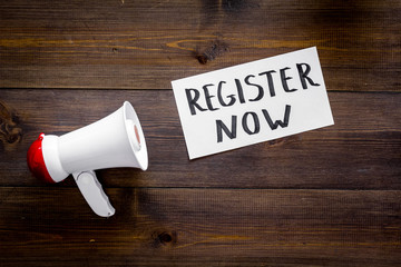 Register now hand lettering icon near megaphone on dark wooden background top view copy space