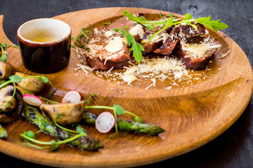 Grilled meat with vegetables in wooden plate on black background