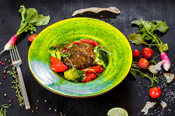meat garnish with vegetables in green plate on black background