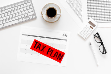 Tax plan words on office work desk with bills, keyboard, coffee, glasses on white background top view copy space