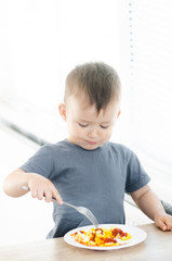 a child in a t-shirt in the kitchen eating an omelet, a fork