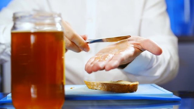 Person spread honey on hand instead on bread close-up 4K. Medium shot of person behind the table in focus while preparing for breakfast, spreading honey on hand in slow motion.