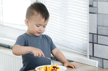 a child in a t-shirt in the kitchen eating an omelet, a fork