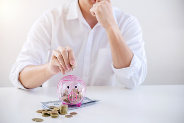 Obraz na płótnie Canvas Businessman putting coins into piggy bank and using calculator to analysis business investment strategy with income of money coin and dollar, financial concept