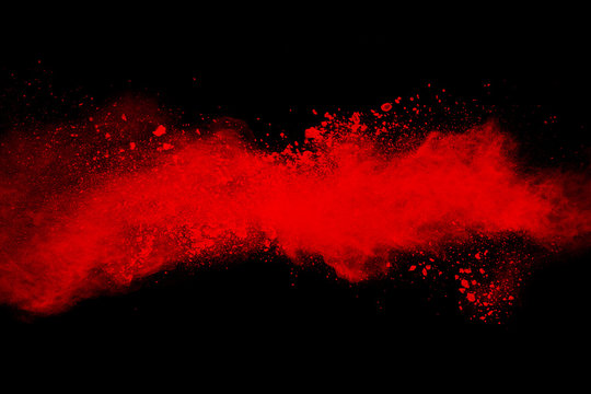 Abstract explosion of red dust  on black background. Abstract red powder splatter on dark  background. Freeze motion of red powder splash.