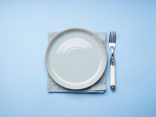 Blue pastel ceramic dish on napkin with fork. Abstract food, tableware crockery concept