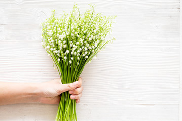 Give a bouquet of delicate lily of the valley flowers. Hand hold bunch of flowers on white background top view copy space