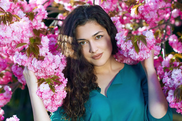 beautiful girl posing near pink sakura flowers as background, face closeup, spring landscape