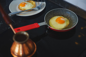 Process of preparing a classic breakfast: fried eggs in a frying pan, a classic Turkish Turk for cooking coffee on a glass hob.