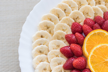 Colorful mix of fresh fruits on a white plate. Orange, banana, strawberry. Vitamins Summer dessert.