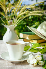 A cup with tea, a laptop, a computer, a bookshine table in the garden on a summer morning, a place to work, a concept of freelancing