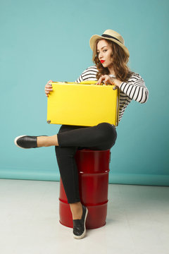 Young happy beautiful woman in summer hat holding yellow suitcase over blue background