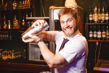 Joyful bartender mixes a cocktail in a shaker