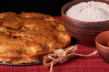 A bowl with flour and apricot cake on a wooden background