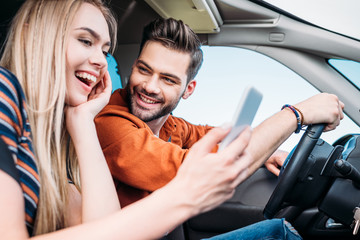 close up view of happy young couple sitting in car with smartphone