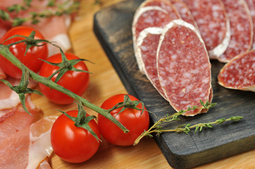Slices of salami on a wooden board. Next a branch of a cherry tomato. Close-up. Macro photography.