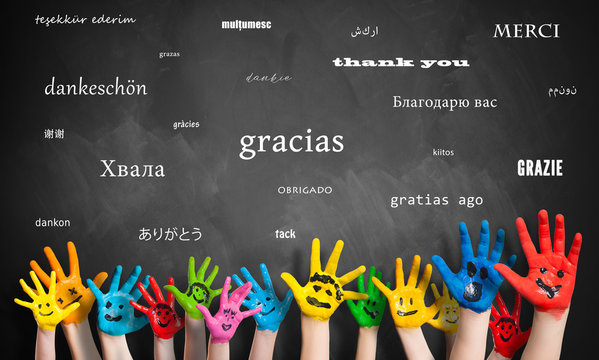 Viele Kinderhände vor Wandtafel mit dem Wort "Danke" in vielen Sprachen