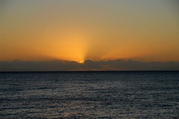 Fototapeta na wymiar ssun setting into dark clouds against orange sky above ocean