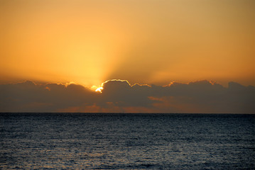 sun setting into dark clouds against orange sky above ocean