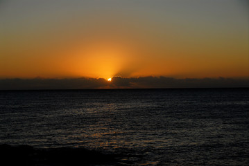 sun setting into dark clouds against orange sky above ocean