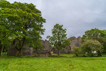 Torlundy, Scotland - June 11, 2012: Ruins of Natural Stone ramparts of Inverlochy Castle near Fort William. Outside view with trees. Green grass and light gray sky.