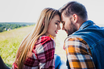 side view of young couple sitting forehead to forehead on car trunk in rural field
