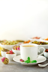 Tea concept with copy space. Different kinds of dry tea in white ceramic bowls and cup of aromatic tea on grey background.