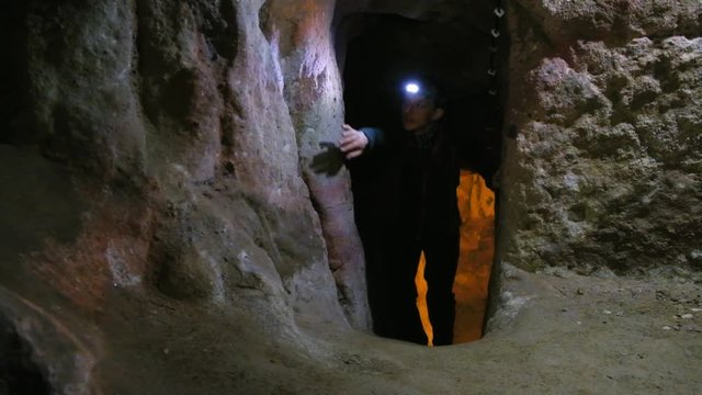 Tourist with lights exploring caves in Kaymakli ancient multi-level underground city, in Nevsehir Province, Cappadocia, Turkey. Interior of rocky room.