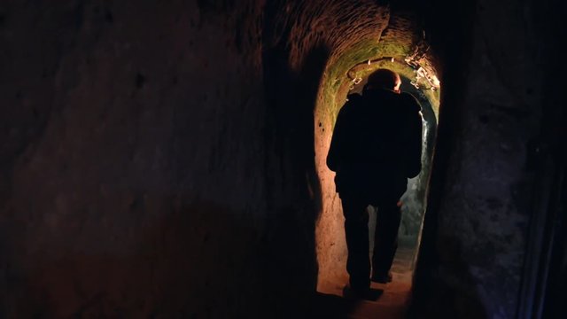 Tourist with lights exploring caves in Kaymakli ancient multi-level underground city, in Nevsehir Province, Cappadocia, Turkey. Interior of rocky room.
