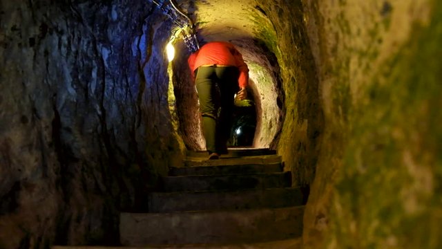 Tourist with lights exploring caves in Kaymakli ancient multi-level underground city, in Nevsehir Province, Cappadocia, Turkey. Interior of rocky room.