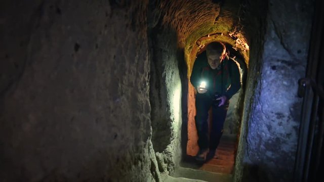 Tourist with lights exploring caves in Kaymakli ancient multi-level underground city, in Nevsehir Province, Cappadocia, Turkey. Interior of rocky room.