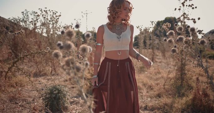 Young woman in boho style walking in autumn wildflowers field