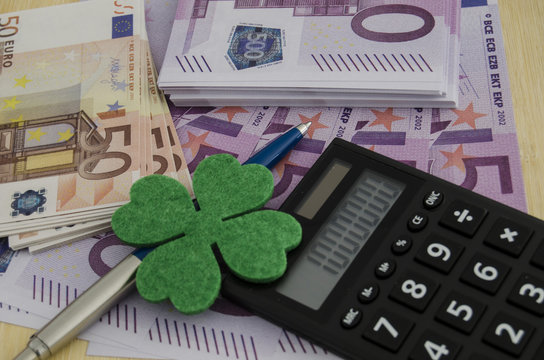 many 500 and 50 euro bills with a four-leaf clover, a pen and a calculator with a miilon of euros