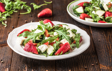Fresh vegetable strawberry salad on white plate on natural rustic desk.