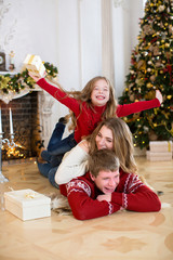 Happy young family lying on top of each other, on floor, on background fireplace and Christmas tree