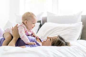 Happy mother with baby lying on bed at home