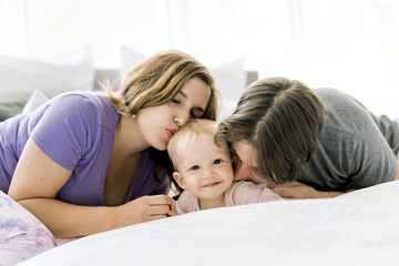 Portrait of beautiful young parents and cute baby on bed