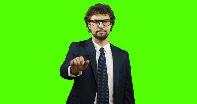 Attractive man in glasses, suit and tie standing on the chroma key background, saying no and doing stop gesture with a hand. Green screen.