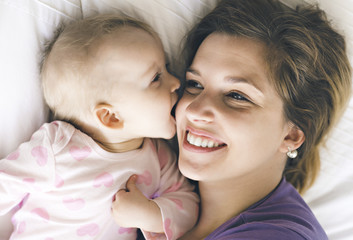 Happy mother with baby lying on bed at home