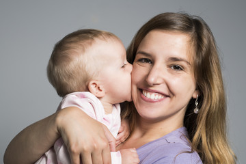 Young mother holding her little baby on studio dark gray